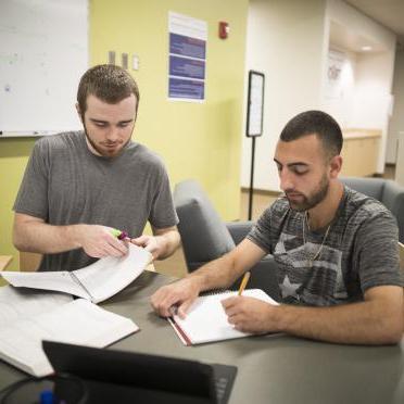 Two male students sit together in the library to study for a paper.
