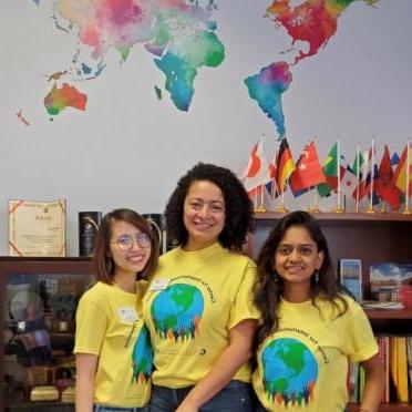 Three students stand under a watercolor map