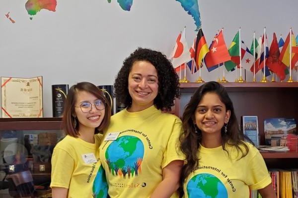 三名留学生穿着印有“国际教育中心”字样的衬衫，面带微笑.