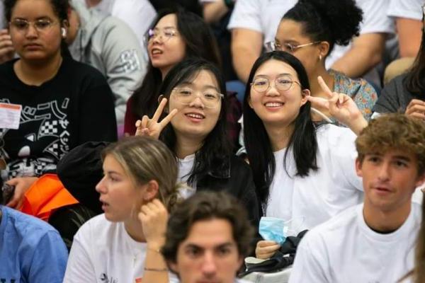 Two international students smile and do a peace sign. 